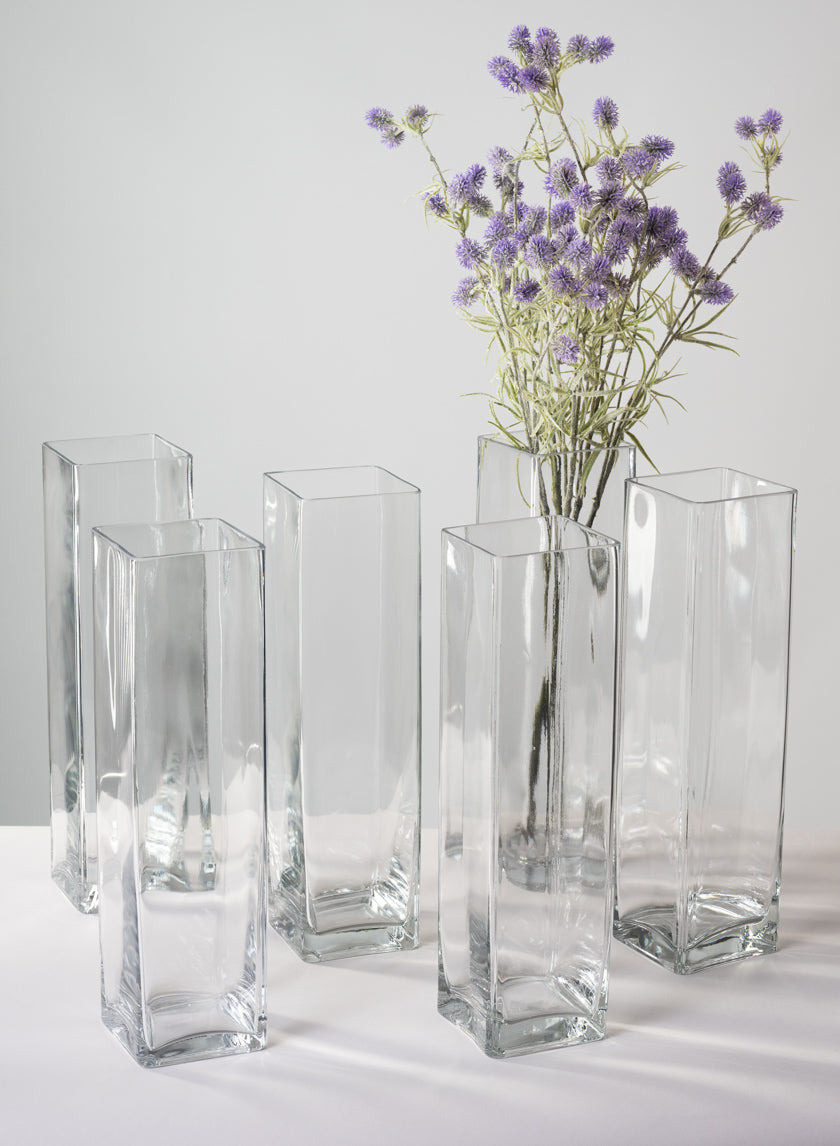 A green glass vase holds three pale green hydrangea blooms with large green leaves, set on a wooden surface against a neutral beige background.