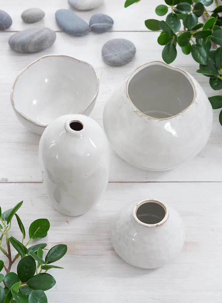 A wooden shelf displays ceramic vases, bowls, and pots in neutral tones. Some hold flowers or small succulents; others are empty. The background is plain and light gray.